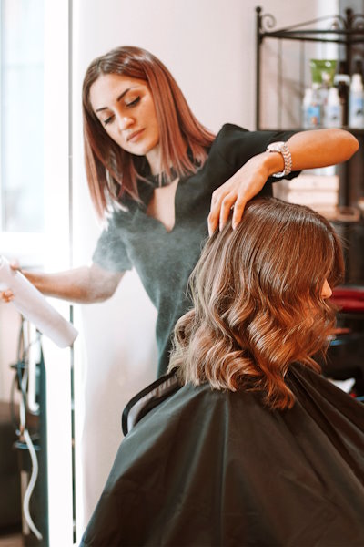 Young,Female,Hairdresser,Fixing,Hair,Of,Gorgeous,Smiling,Woman,With